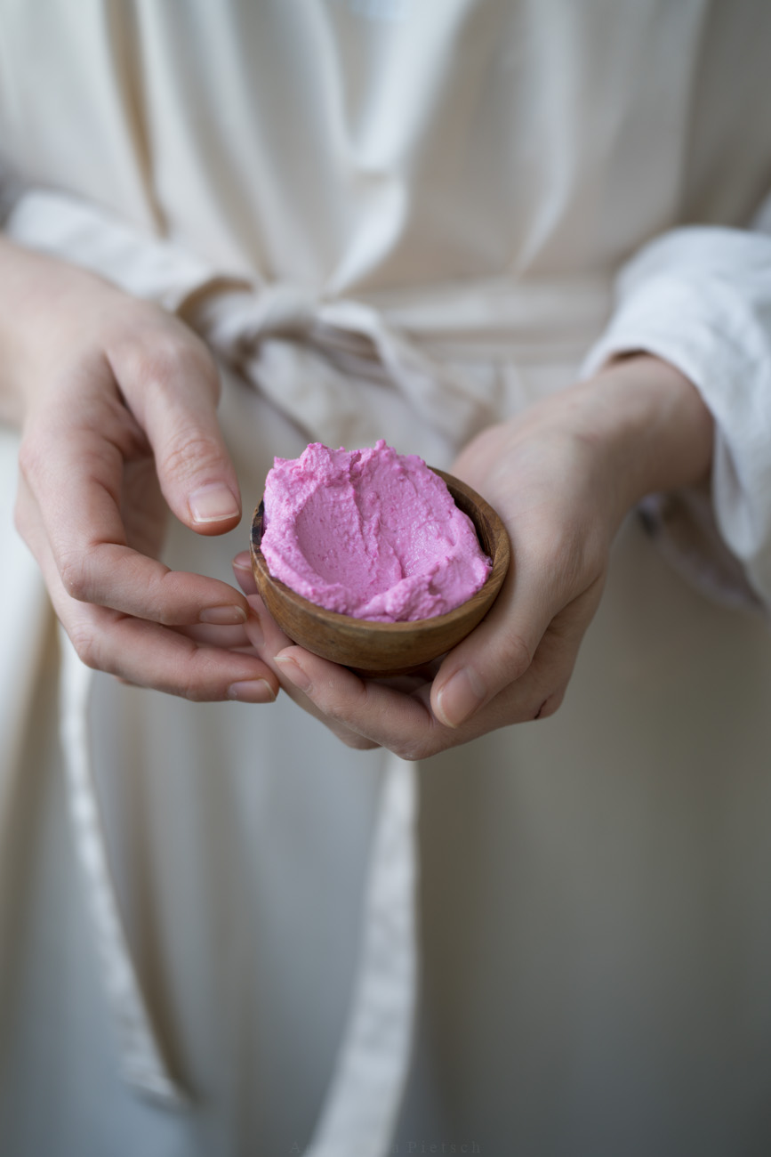Eine Person mit einer beigen Schürze hält ein Schälchen mit pinker Feta-Creme in der Hand.