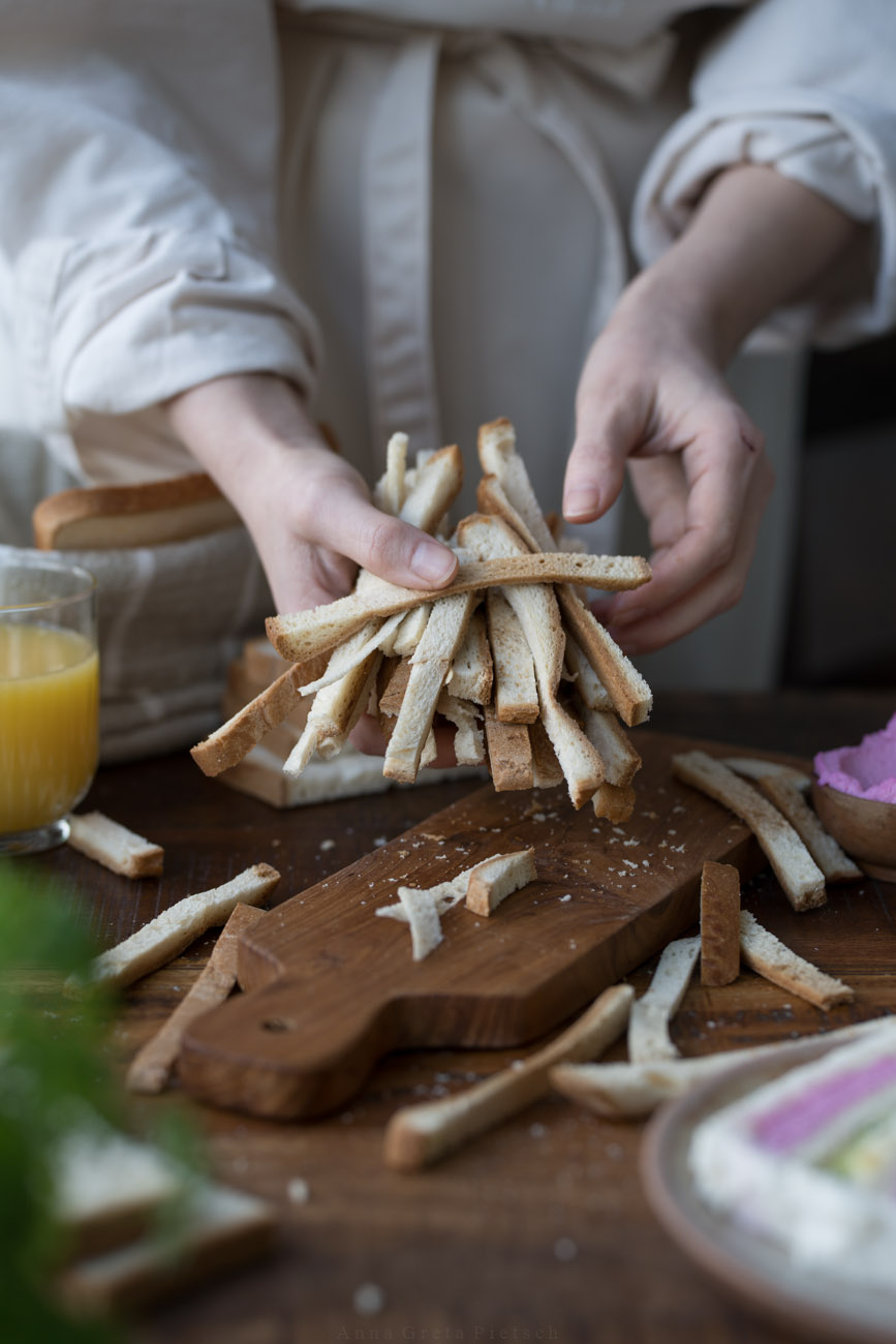 Eine Person mit einer beigen Schürze hält abgeschnittene Toast-Ränder in der Hand.
