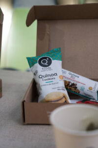 Ein kleiner Pappkarton mit Snacks aus Quinoa steht auf einem Tisch.