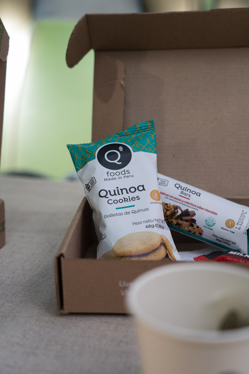 Ein kleiner Pappkarton mit Snacks aus Quinoa steht auf einem Tisch.