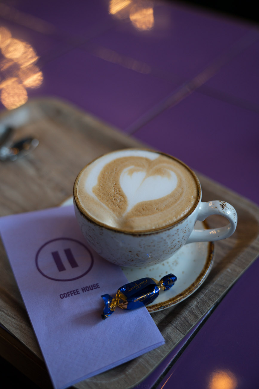 Eine Tasse Kaffee auf einem Holztablett. Die Tischplatte darunter ist lila.