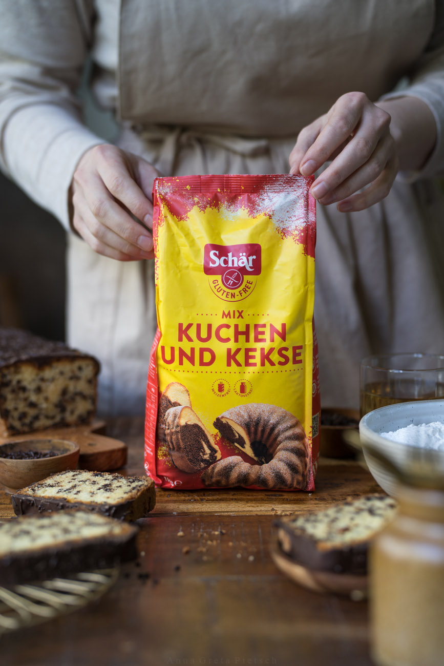 Eine Arbeitsfläche, in der Mitte wird ein Paket mit glutenfreiem Mehl von zwei Händen gehalten.