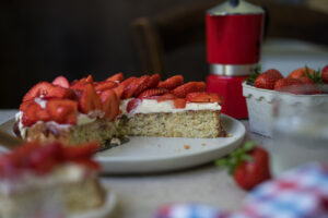 Ein angeschnittener Erdbeerkuchen steht auf einem gedeckten Tisch.