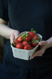 Eine Person hält eine Pappschachtel mit Erdbeeren in den Händen.