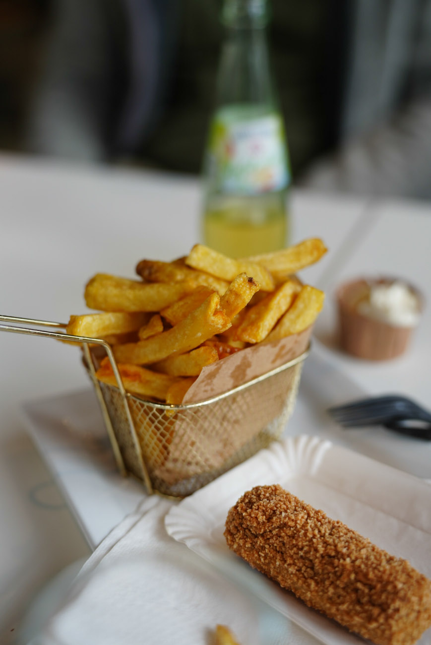 Pommes in einem Metallkörbchen. Davor liegt eine frittierte Krokette.