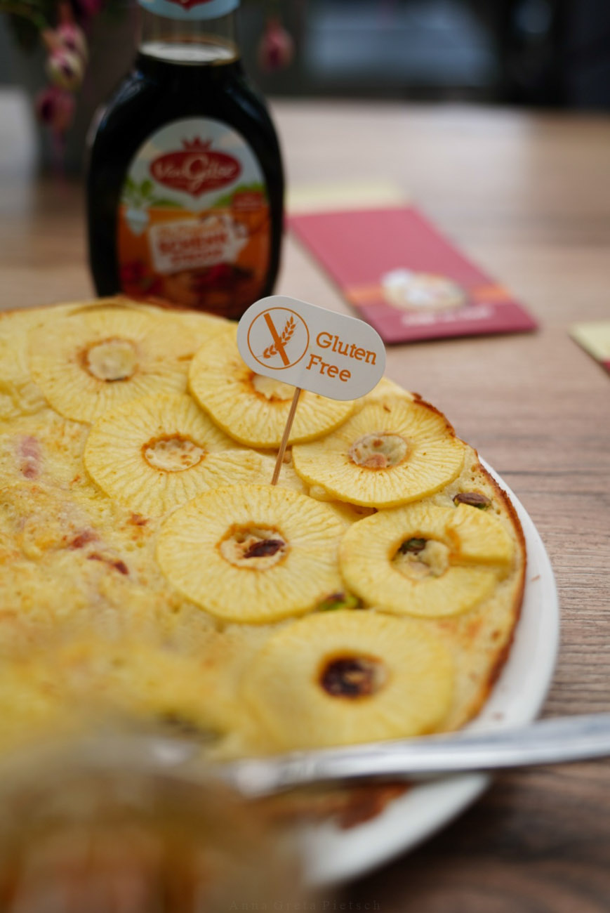 Pfannekuchen auf einem Teller mit Apfelscheiben belegt. Im Hintergrund sieht man eine Sirupflasche.
