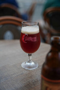 Ein Glas mit Bier steht auf einem Tisch. Man sieht die Bierflasche im Anschnitt.
