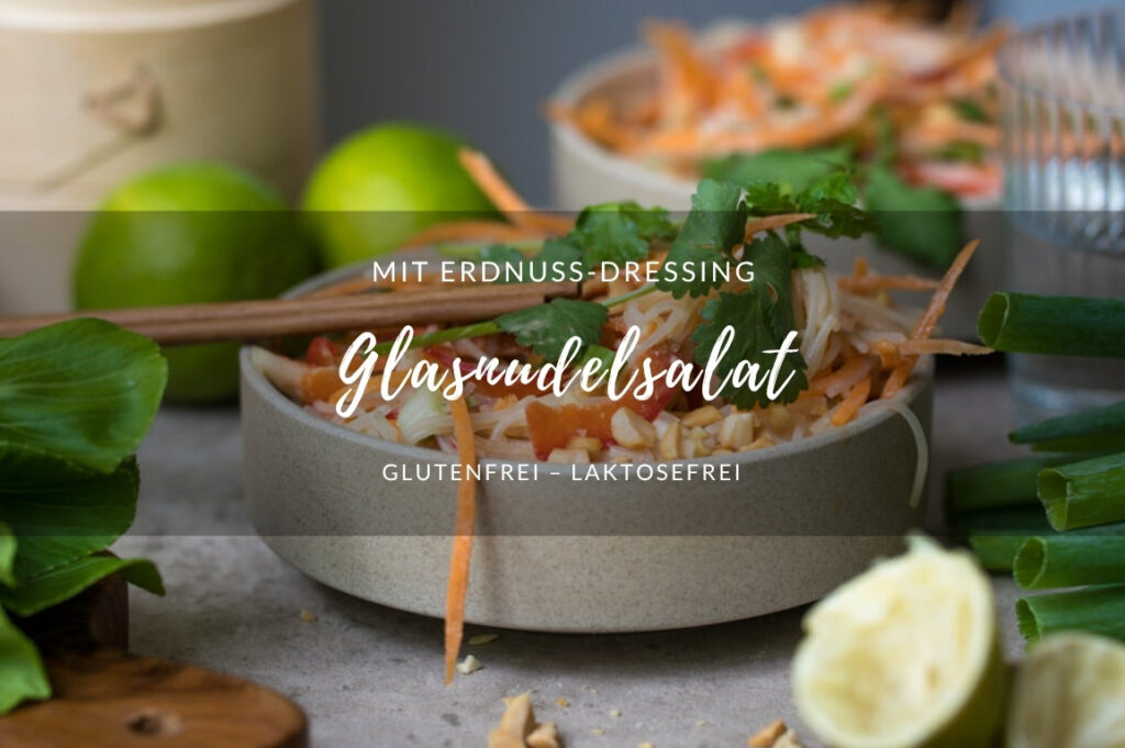 Glasnudelsalat mit Erdnuss-Dressing Glasnudelsalat mit Erdnusssoße in einer beigen Keramikschale auf einem Tisch. Im Hintergrund steht eine weitere Schale. Sonst sieht man ausgepresste Limetten im Vordergrund, Pak Choi am Rand, Wassergläser auf dem Tisch.