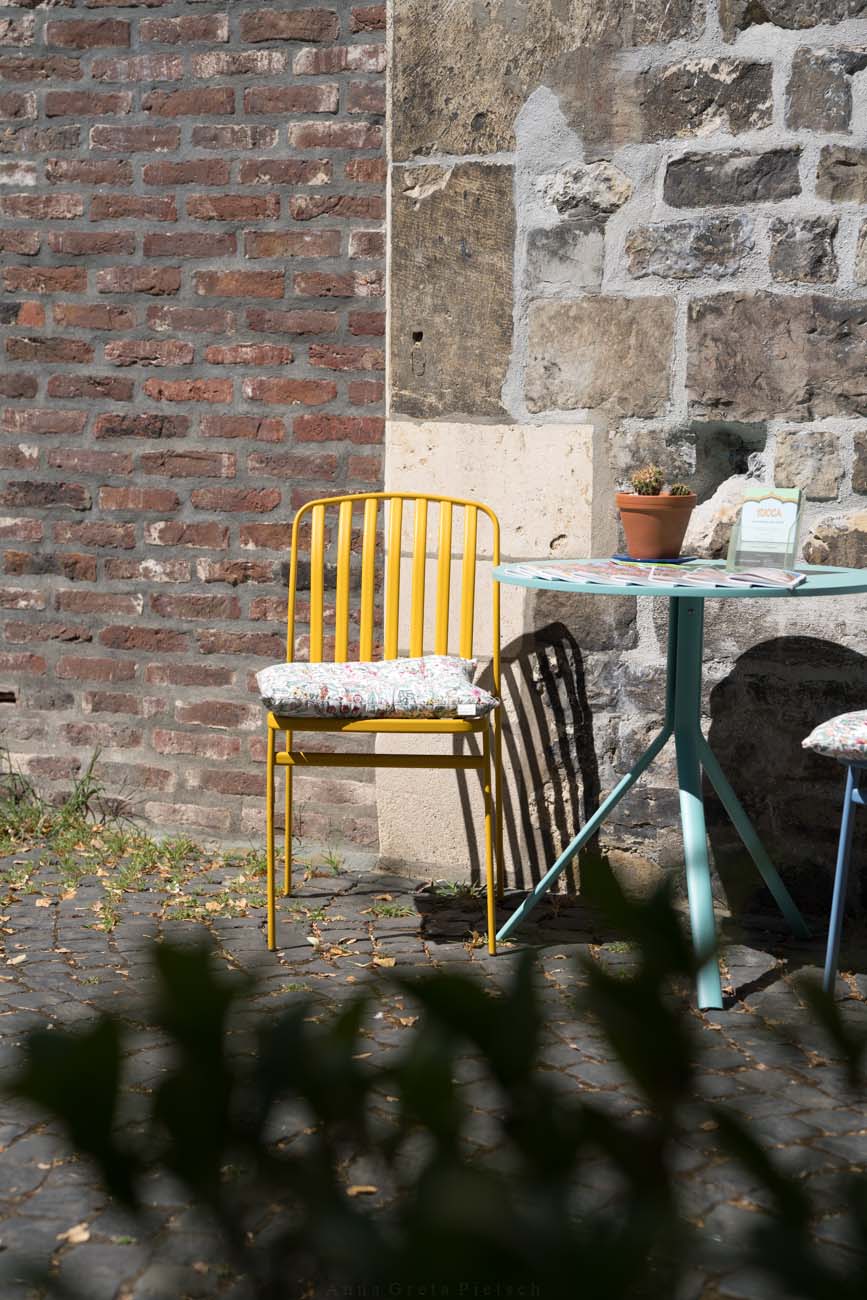 Ein gelber Metallstuhl neben einem Tisch in der Altstadt von Aachen.