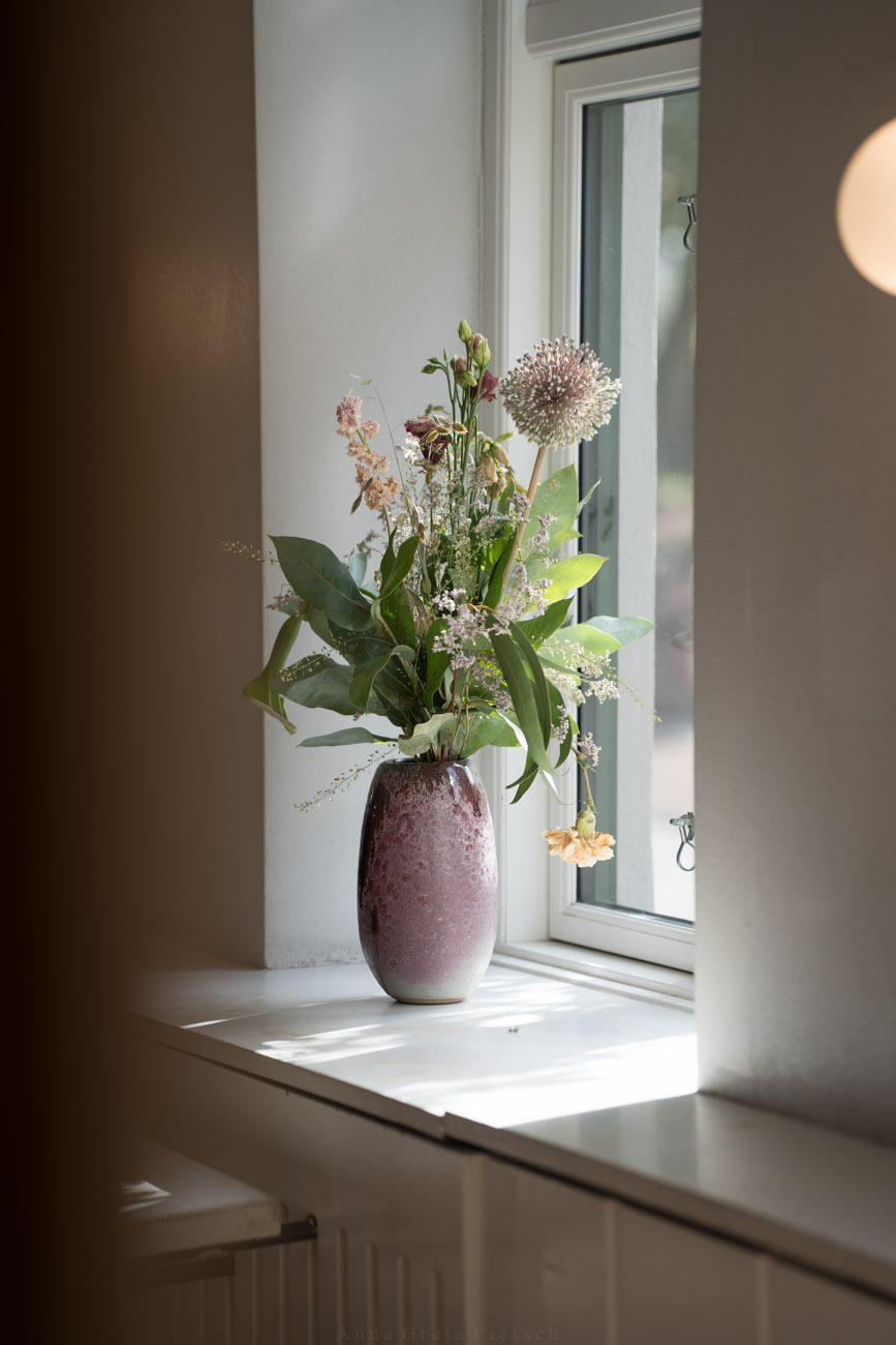 Eine große Blumenvase in einem Lichtdurchfluteten Fenster mit frischen Blumen.