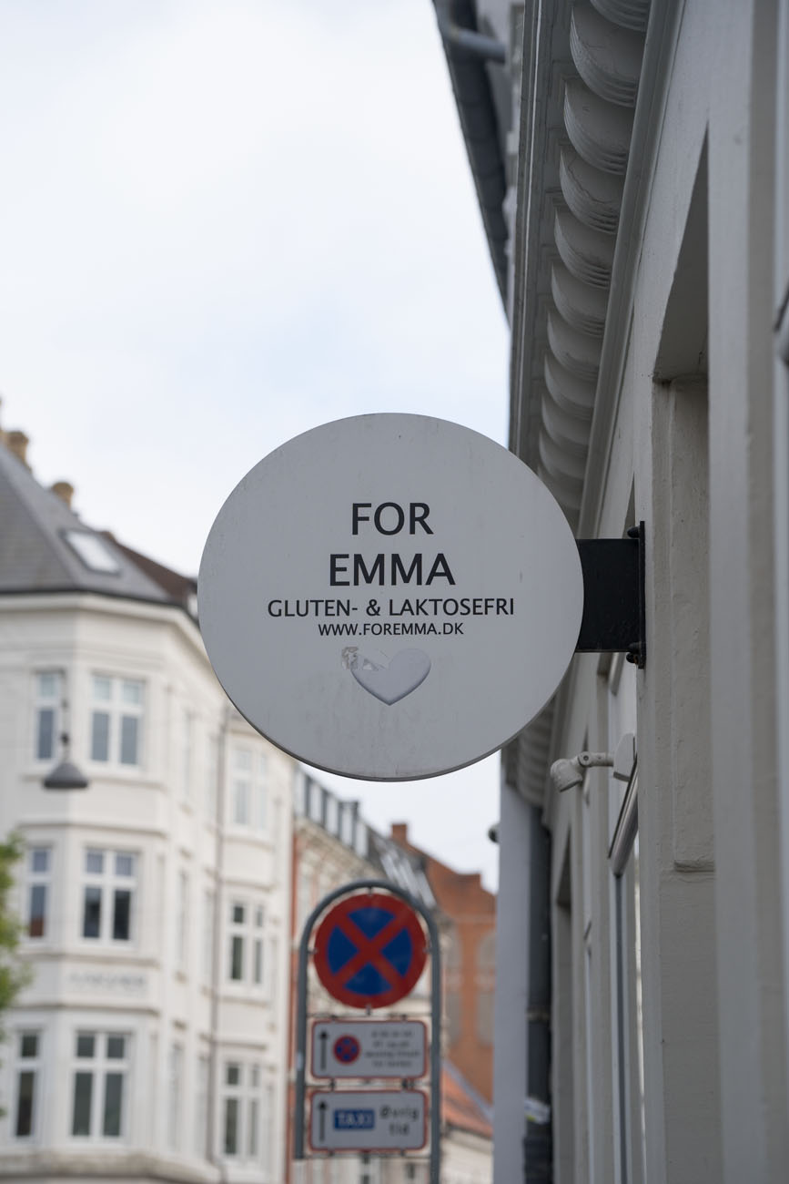 Ein rundes Schild an einer Hausfassade mit dem Namen der Bäckerei "For Emma" in Aarhus, Dänemark.