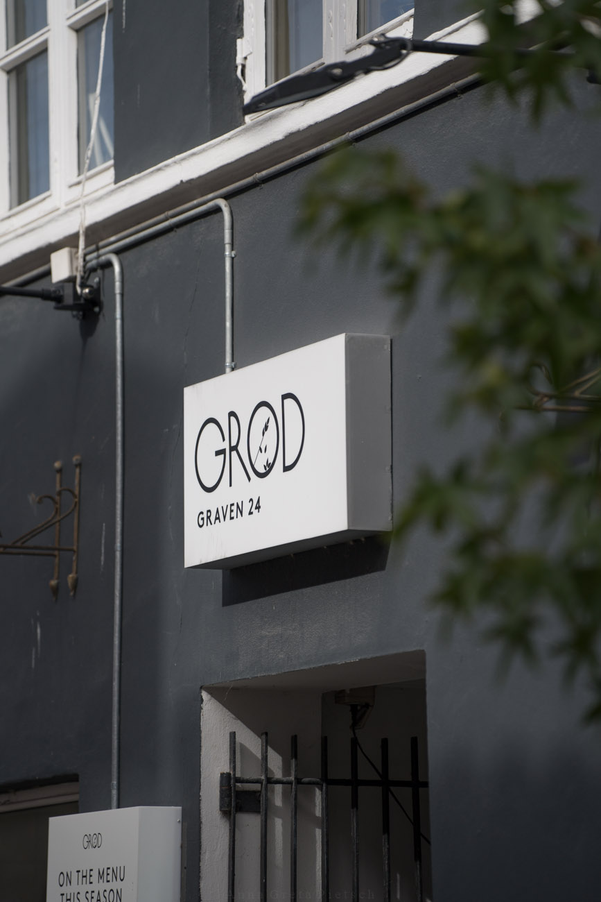 Ein Schild an einer schwarzen Hauswand mit dem Namen des Lokals "Grød".