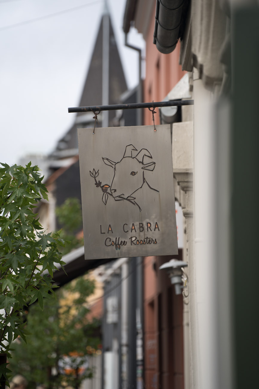 Ein Schild an einer Hausfassade mit dem Namen des Cafés "La Cabra" darüber ist eine Ziege eingraviert, das Markenzeichen des Cafés.