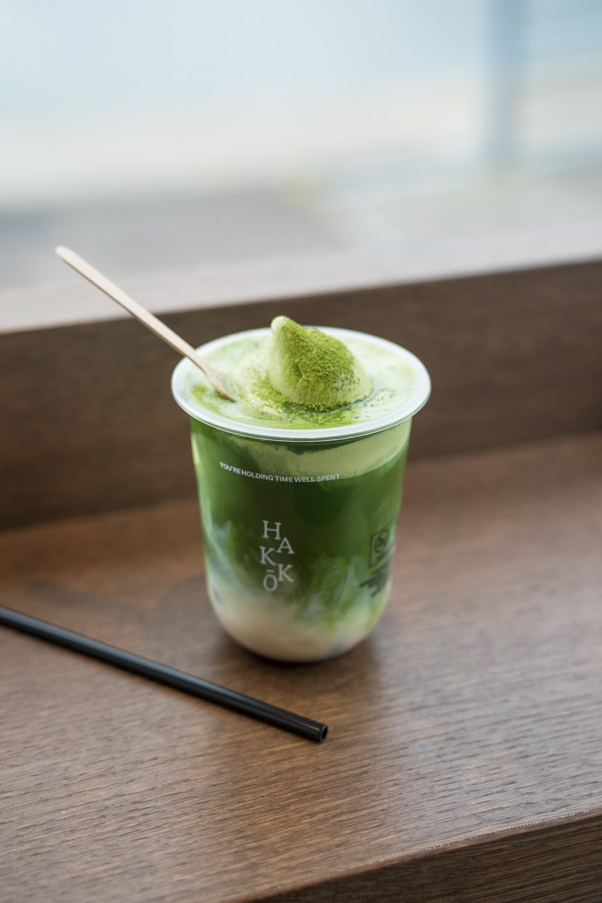 Ein grüner Matcha bei Hakko in Aarhus, Dänemark in einem Plastibecher auf einer hölzernen Ablage.