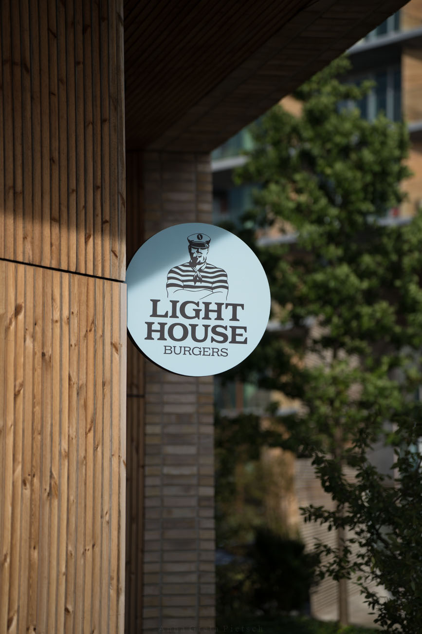 Ein hellblaues Schild an einer hölzernen Hausfassade mit dem Namen des Restaurants "Lighthouse Burgers" in Aarhus, Dänemark.