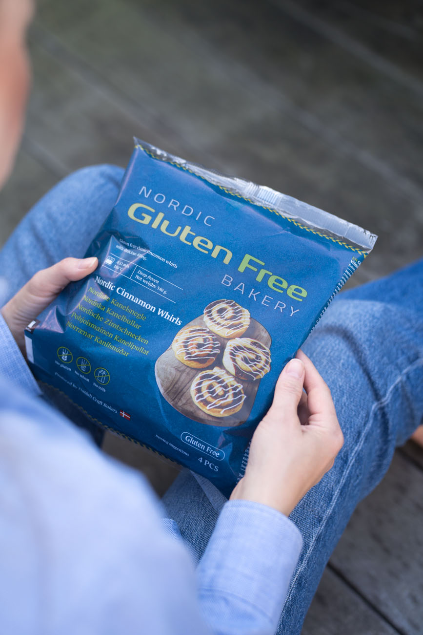 Eine Person hält ein Paket mit glutenfreien Zimtschnecken zum Aufbacken in den Händen.