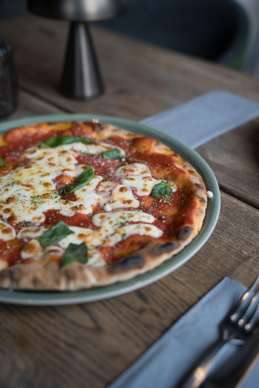 Eine Pizza auf einem großen Teller auf einer Holztischplatte.